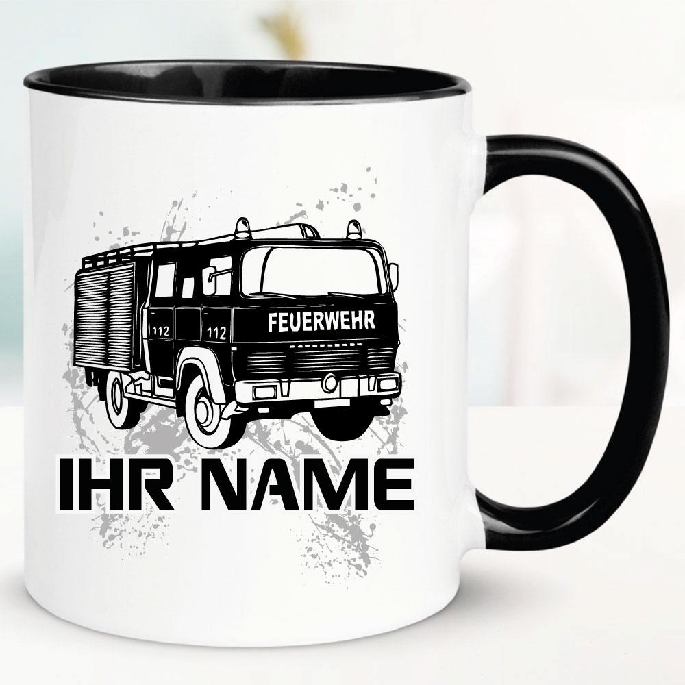 Schwarze Tasse mit Feuerwehrauto und Name bedruckt.